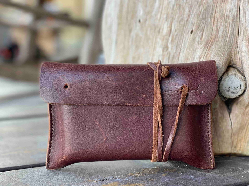 Dark brown full-grain leather wallet with natural scuffs and a tied leather cord leaning against rustic weathered wood.