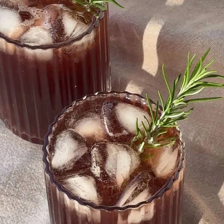 Two glasses of iced dark beverage with rosemary garnish.