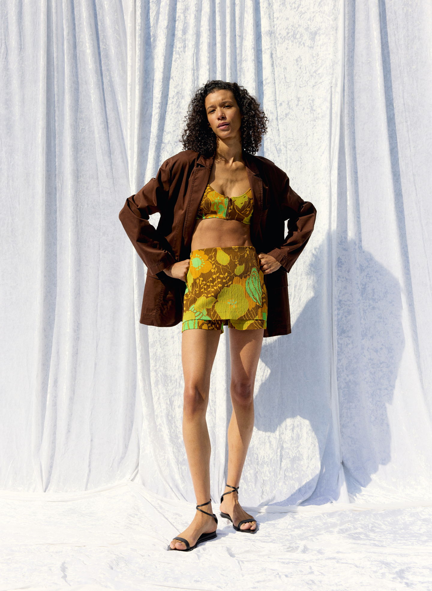 Model wearing colorful outfit with a brown jacket against a textured background.