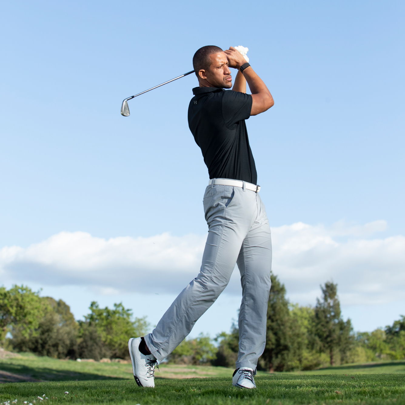 Golfer swinging a club on a sunny day at a golf course.
