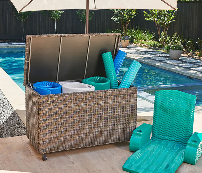 Storage box with pool accessories beside a swimming pool and lounge chair.