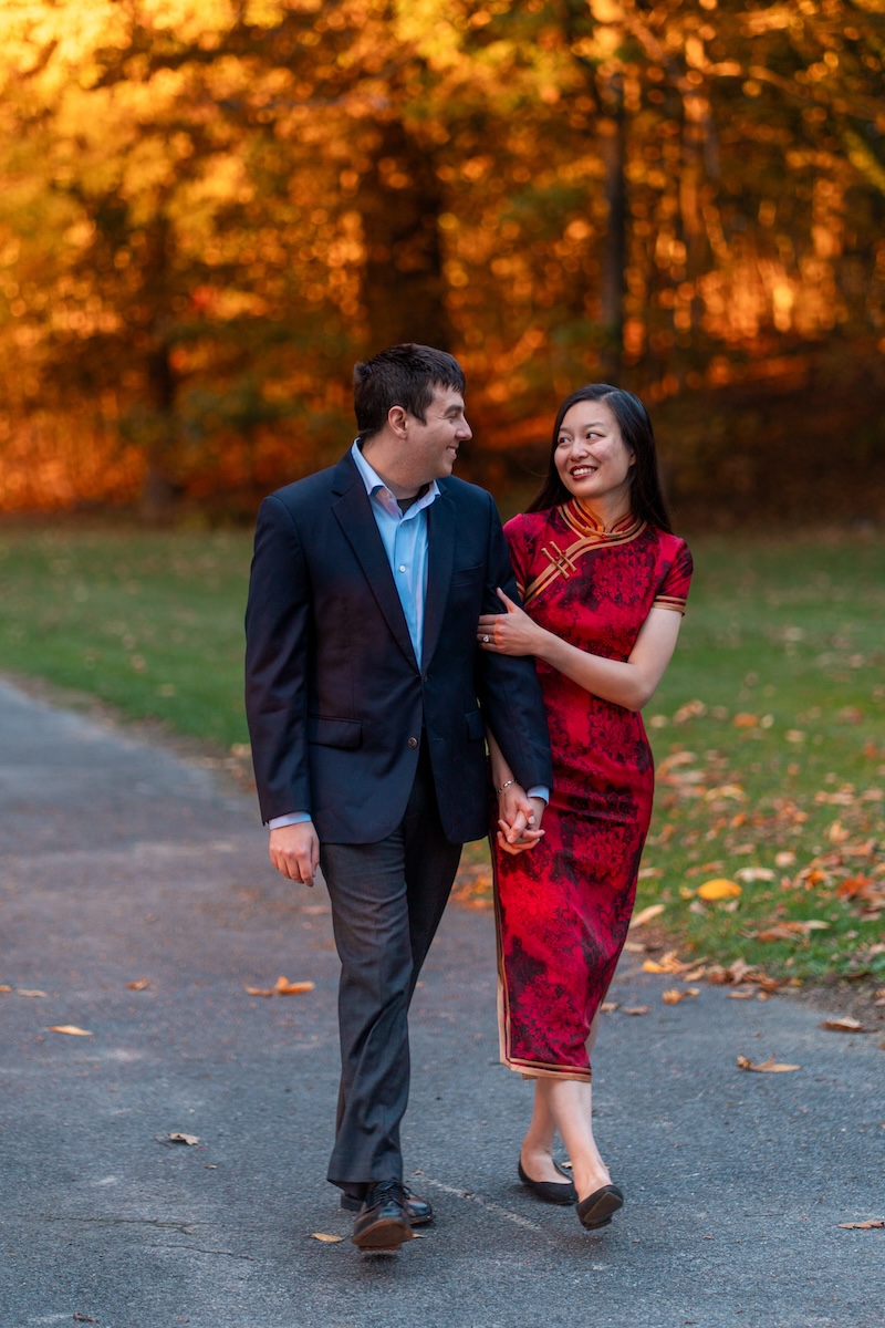 engaged couple walking in front of fall foliage