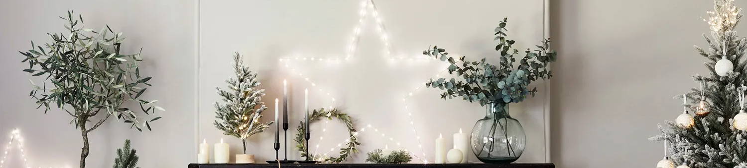Festive fireplace in living room with oversized Osby star light illuminated on mantel with variety of festive foliage and mini trees with an assortment of TruGlow candles displayed