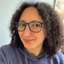 Person with curly hair and glasses smiling at the camera.