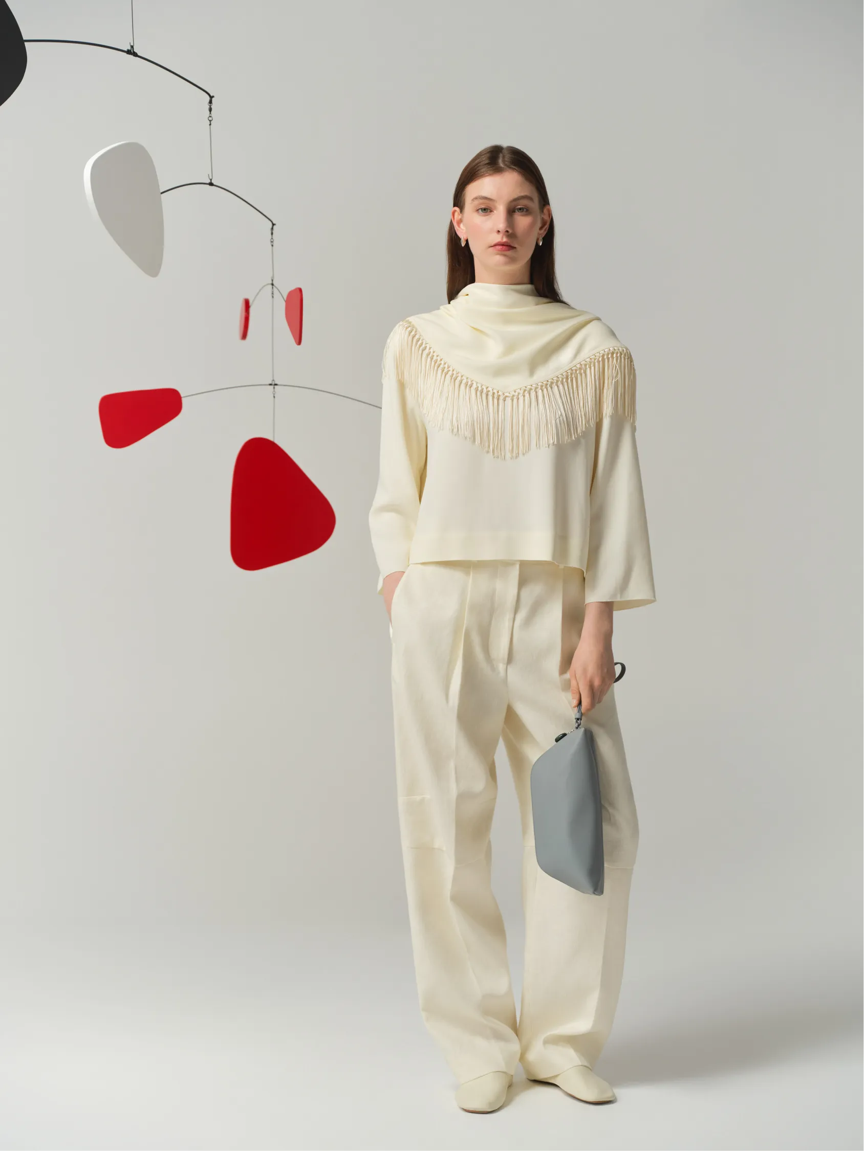 A model in a cream outfit stands against a minimalist backdrop.