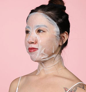 Woman wearing a facial mask against a pink background.