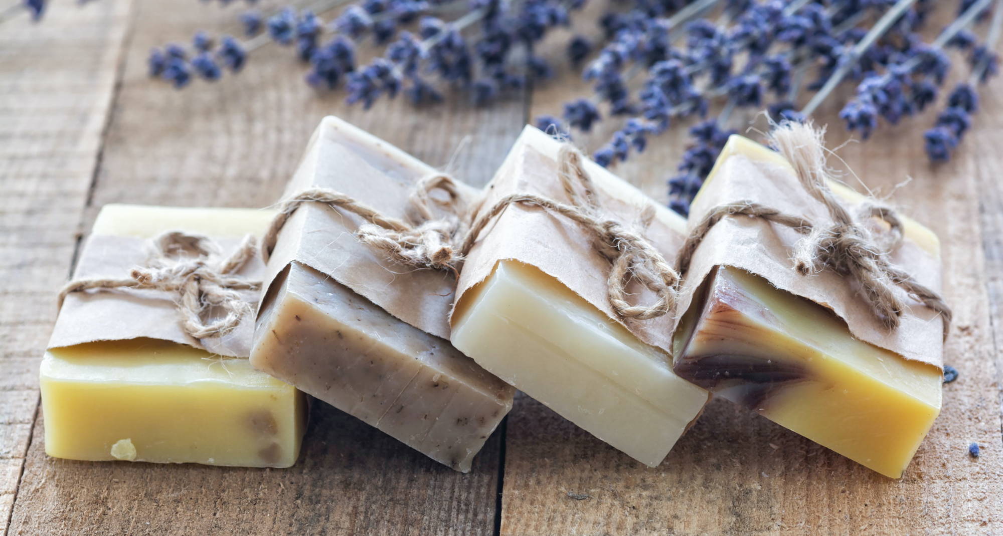 Four bars of twine and paper-wrapped hemp soap with sprigs of lavender on wooden boards.