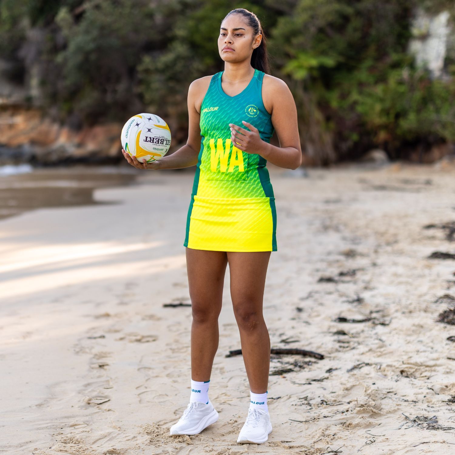 A netball player standing on a beach holding a ball.