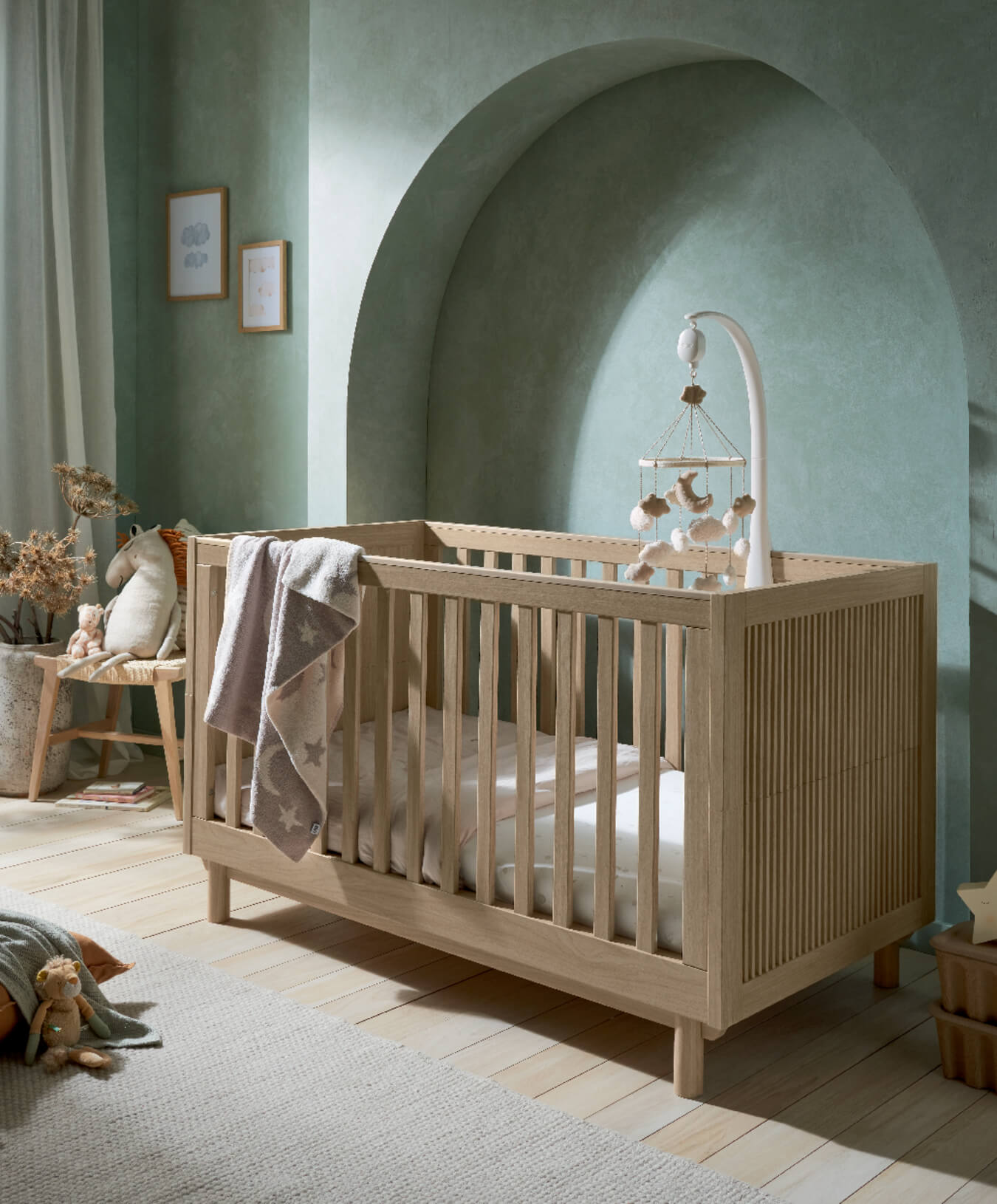 Wooden crib in a softly lit nursery with green walls and decorative elements.