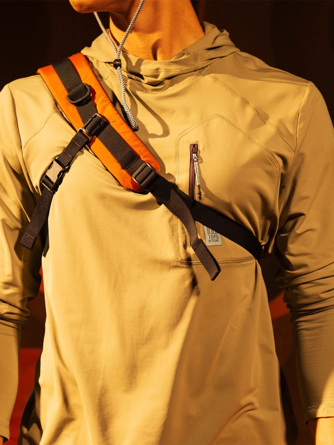 Person wearing a beige hoodie with a black and orange shoulder strap.