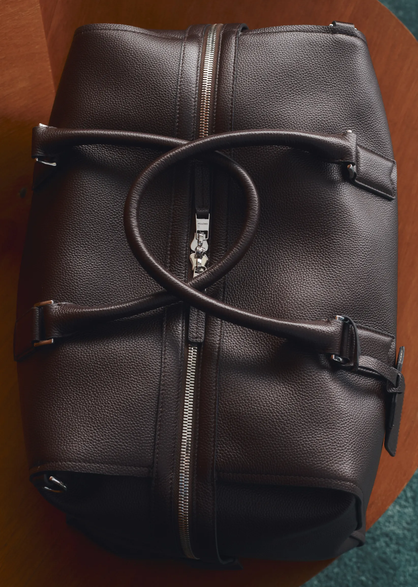 A brown leather bag with straps, resting on a wooden surface.