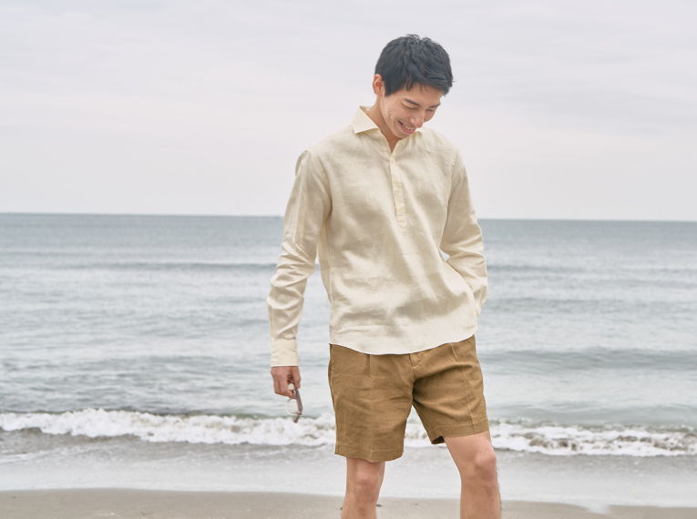 Person in light hoodie and shorts standing on beach by the ocean.
