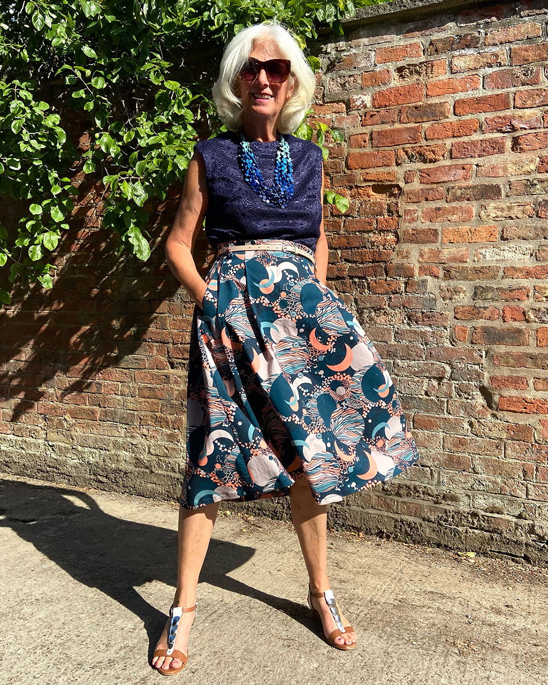 Elderly woman in stylish outfit poses against a brick wall.