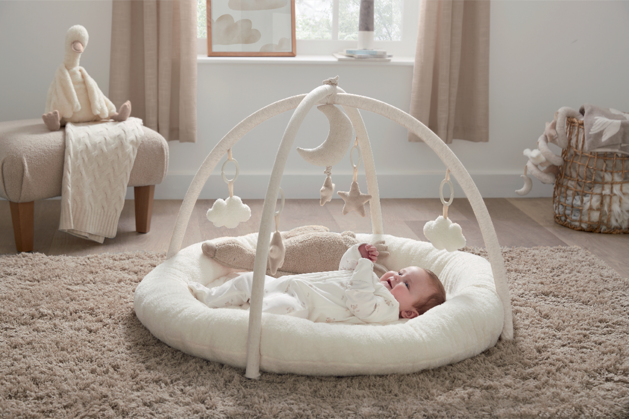 Baby lying on a soft mat under a play gym in a cozy room.