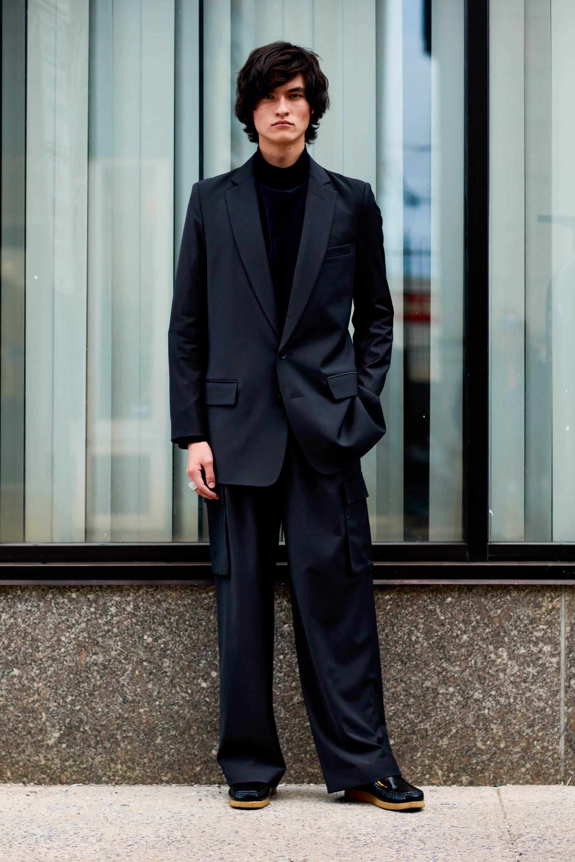 Man in a black suit standing in front of a glass wall.