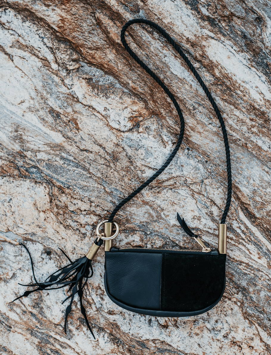 black zip leather crossbody on a rock
