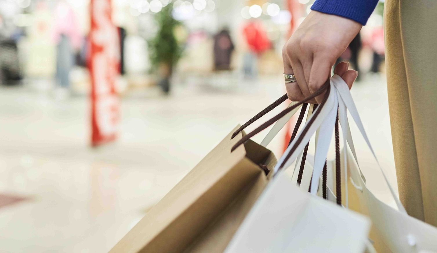 A hand holding multiple shopping bags in a store.