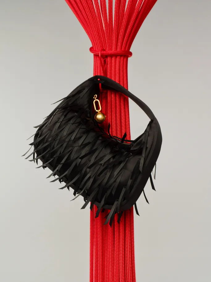 Black handbag with fringe hanging from a red structure.