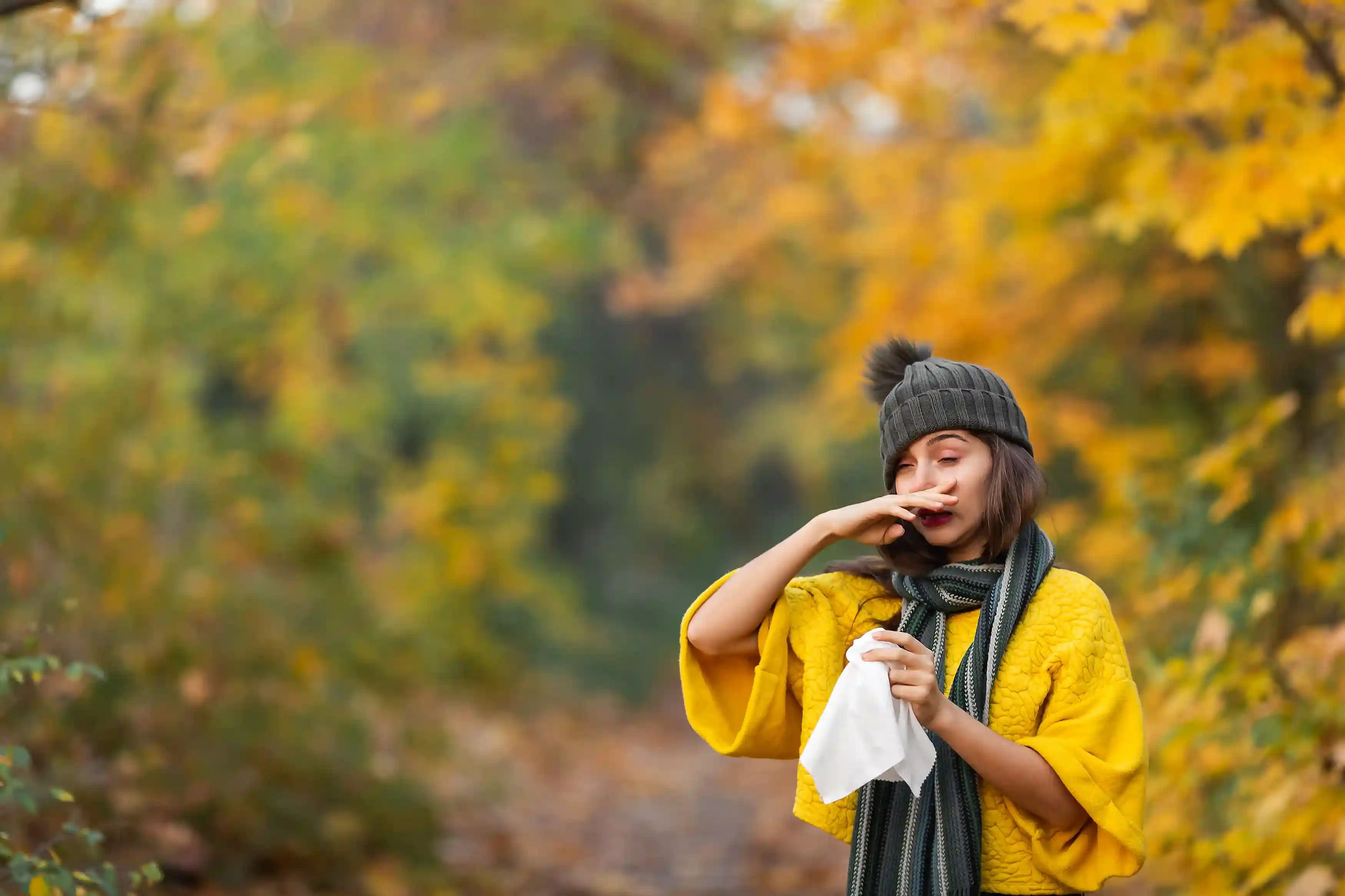 Een vrouw in een herfstbos moet niezen, ze reageert op de pollen in de lucht. Boompollenallergie is een veelvoorkomende allergie die veel niezen of een verstopte neus veroorzaakt.