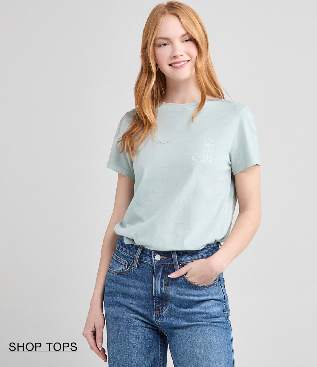 Smiling woman in a light blue shirt and jeans, standing against a neutral background.