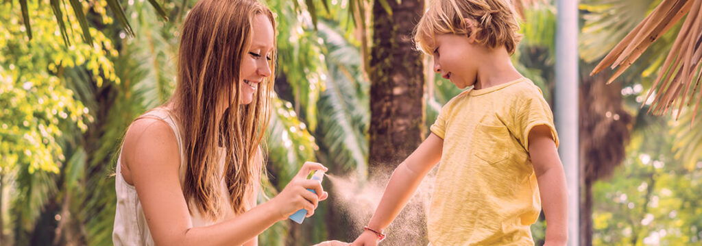A woman applying sunscreen on a child's arm outdoors.