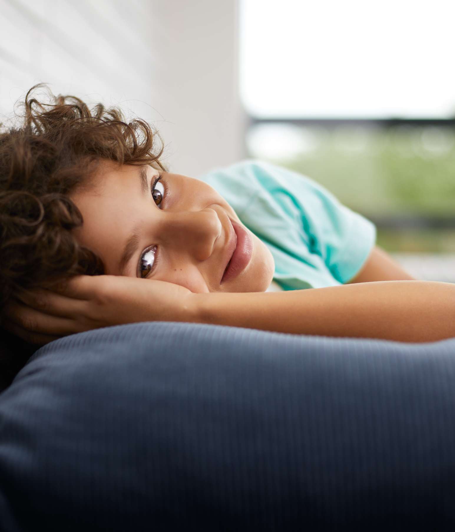 Boy lying on his sofa with his arm under his head – it’s daytime and he’s missing school again because of his allergies