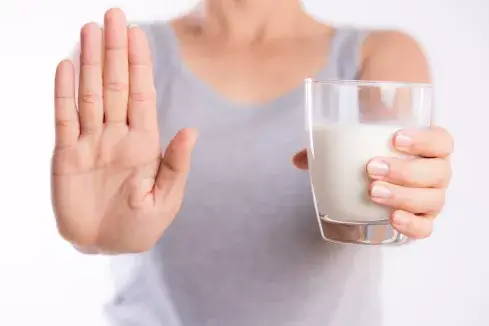 Een vrouw met een glas melk maakt een soort stop-gebaar met haar hand