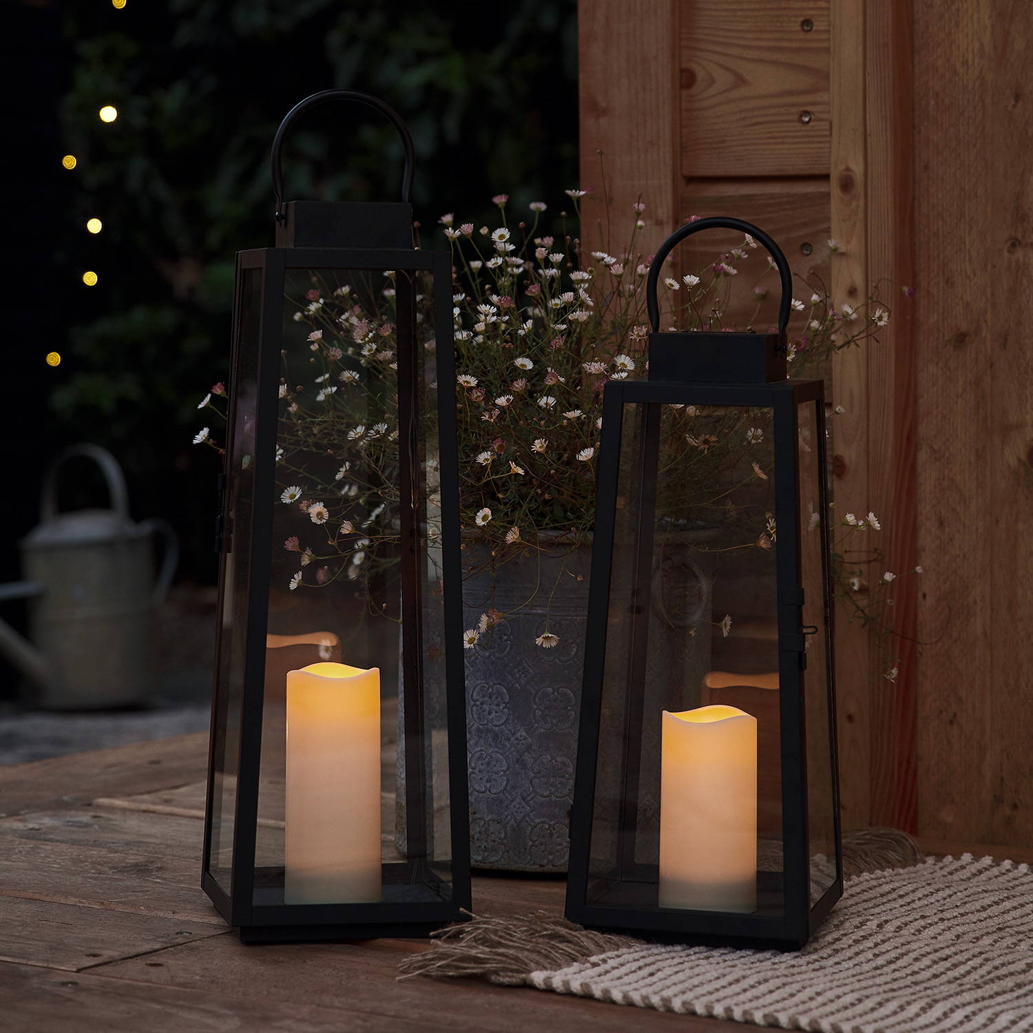 2 trapeze solar lanterns with solar candles outside of a wooden summer house.