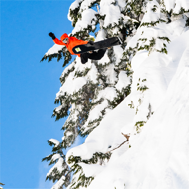 A snowboarder in an orange jacket jumps off a snowy slope.
