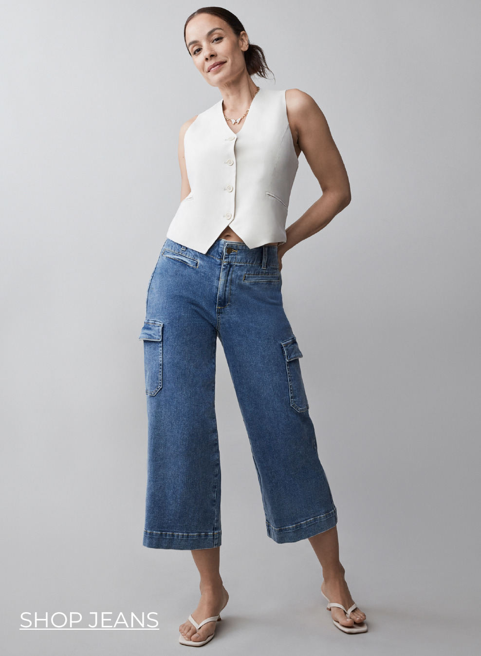 Woman posing in a white top and blue wide-leg jeans.