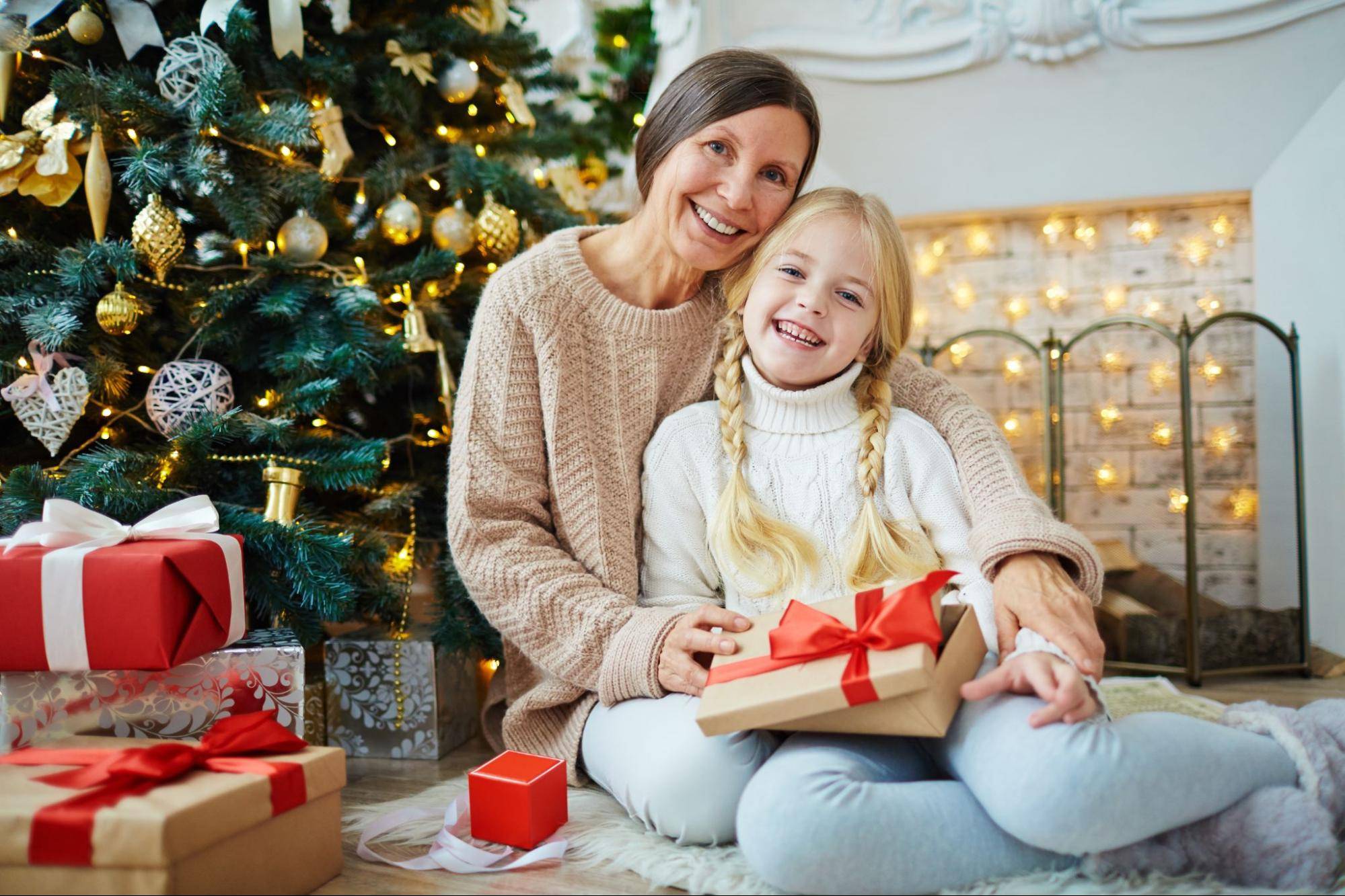 daughter holding presents on mom's lap in front of Christmas tree