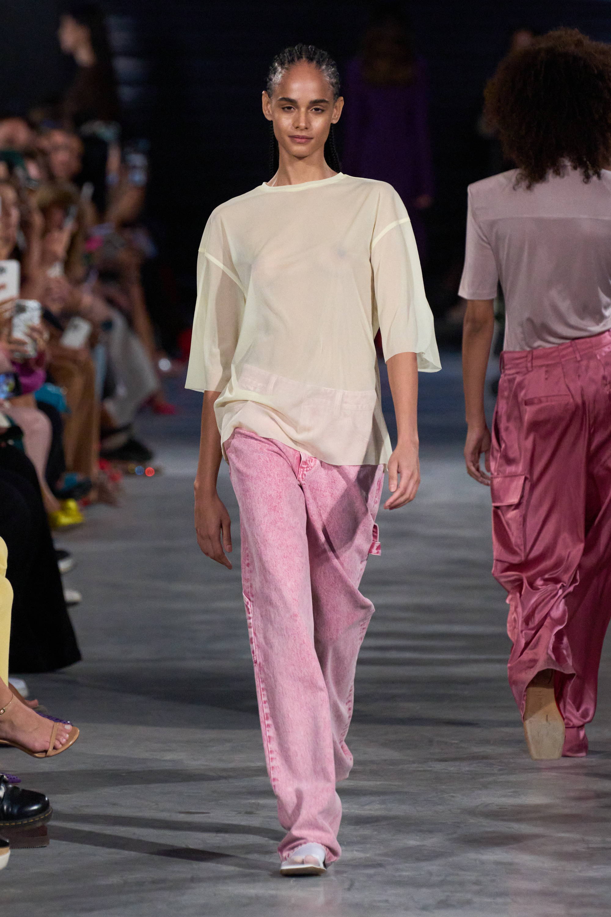 Model on a runway wearing sheer t shirt and jeans