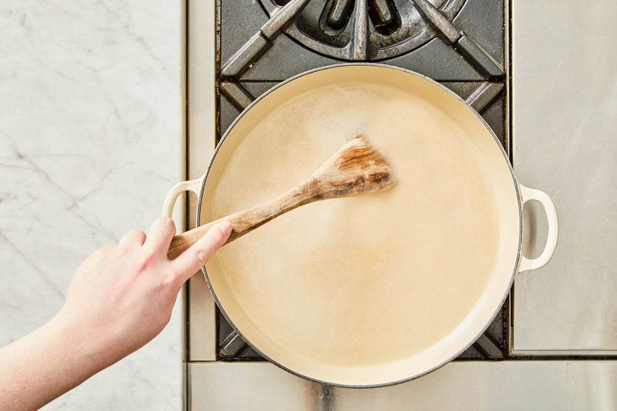 Hand stirring a pot of boiling water with a wooden spoon