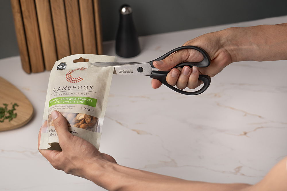 A person using Signature Scissors to open a food package on a countertop.