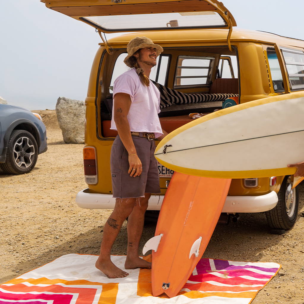 Person standing on Rumpl Everywhere Mat next to van and surfboard