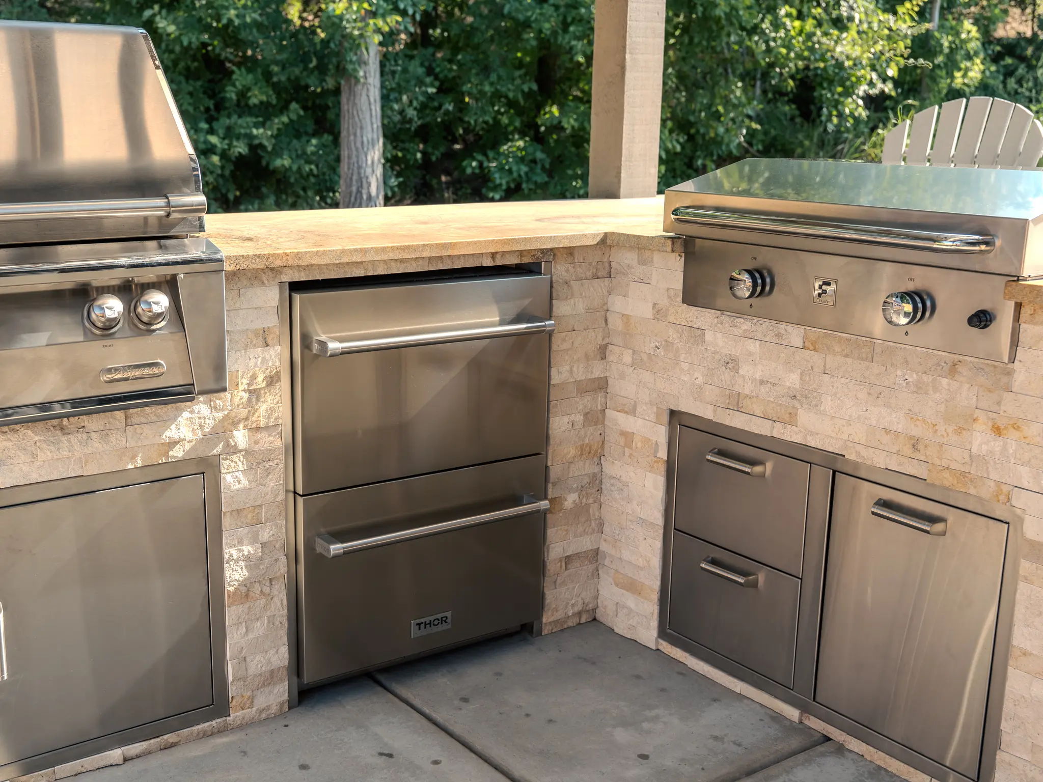 Outdoor kitchen with stainless steel grill, refrigerator, and storage cabinets.