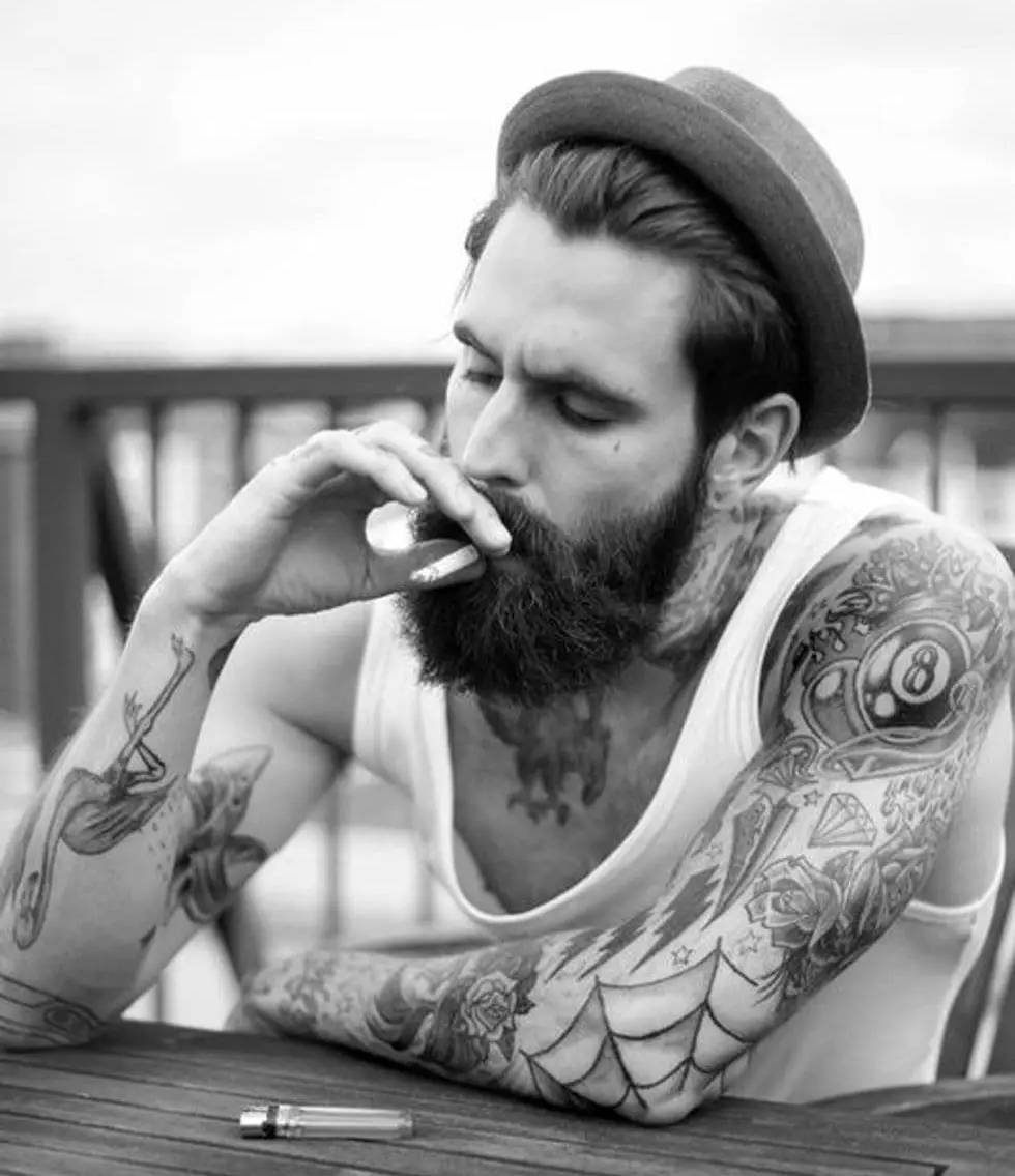 Hipster man whose facial hair is longer than the actual hair with a full-sleeve tattoo