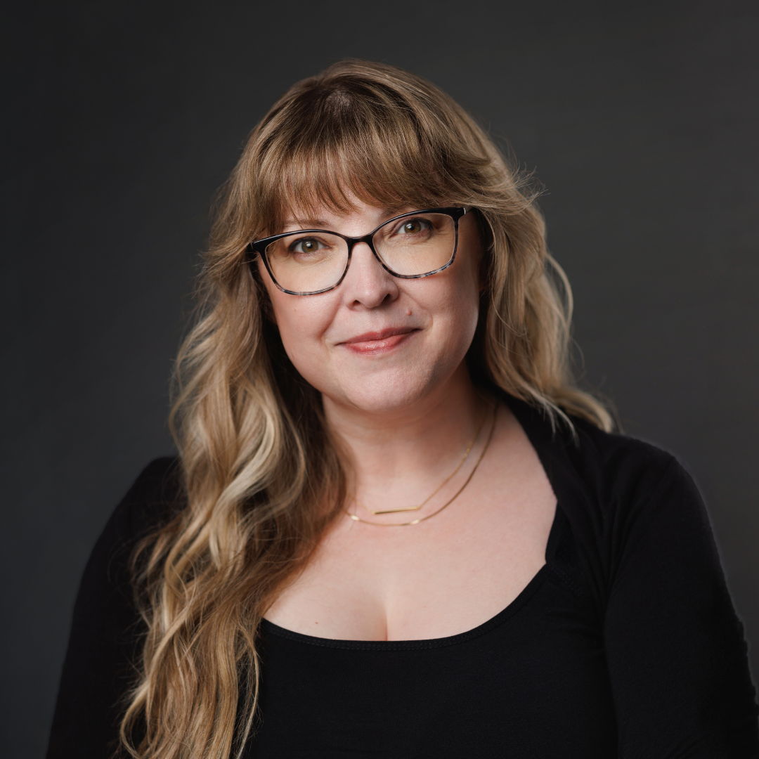 Woman with glasses and long hair, wearing a black top, smiling.
