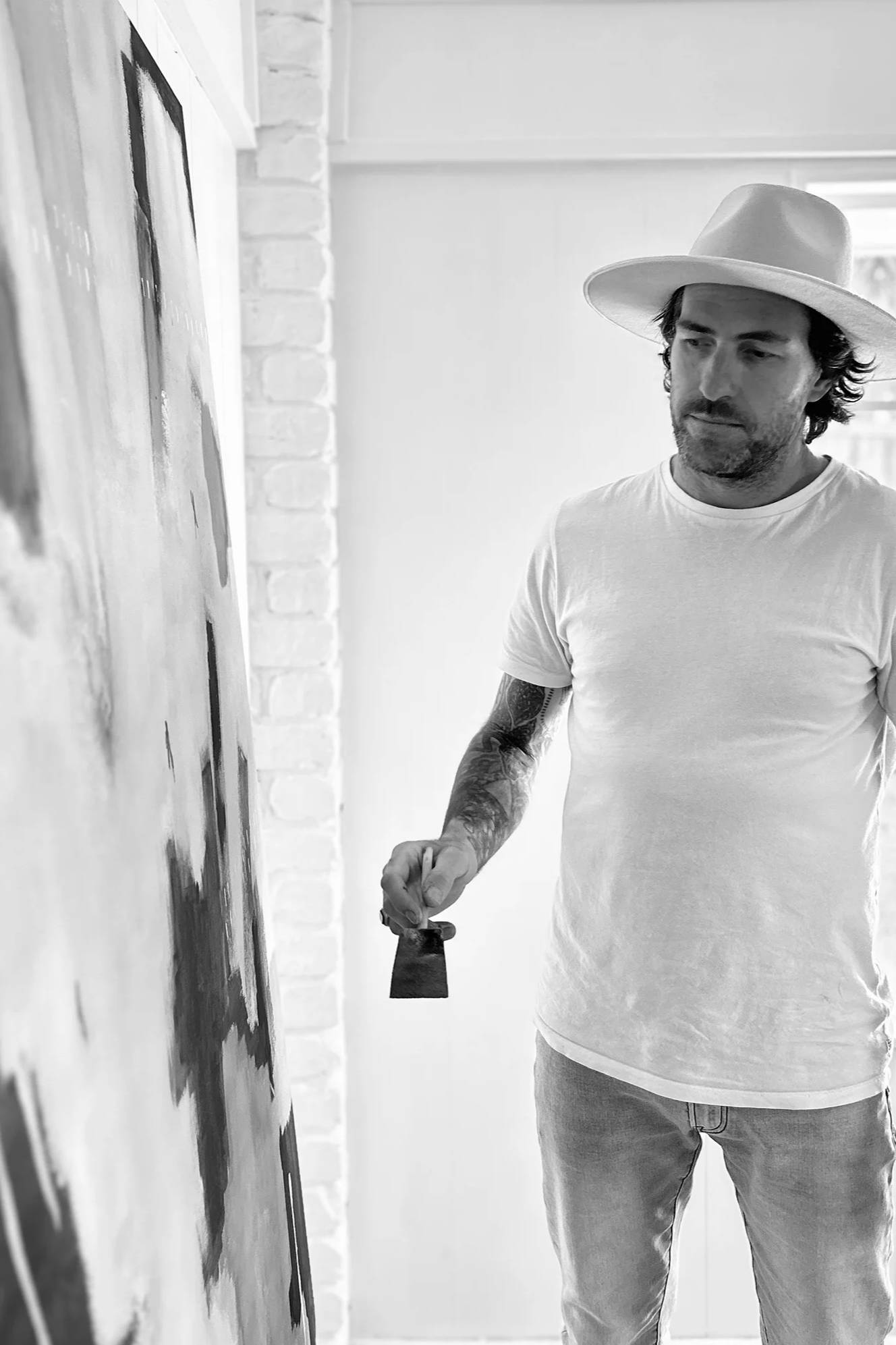 Stephen Skinner in a hat painting on a canvas in a bright room.