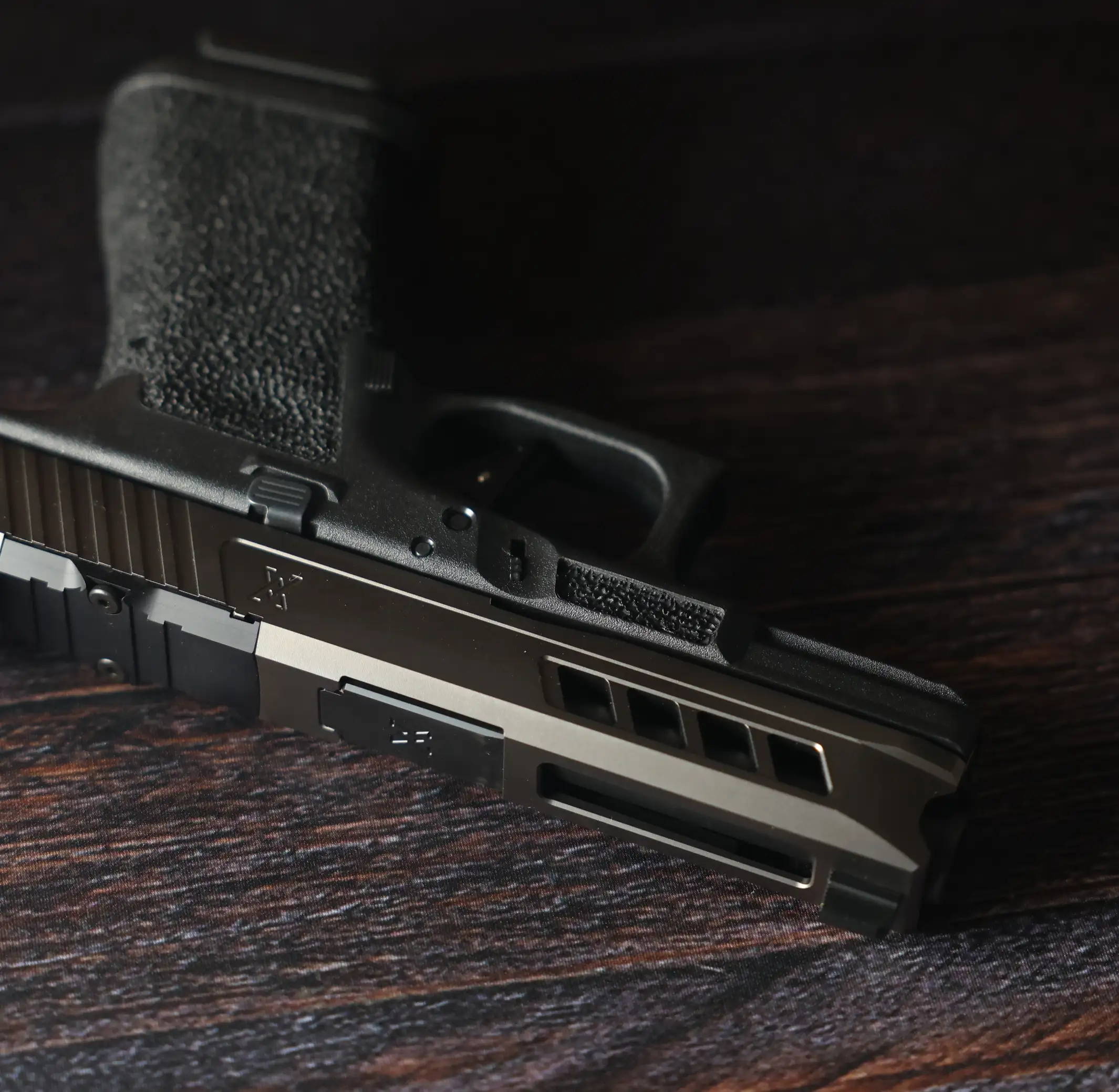 Glock 19 with Grey True Precision Slide and Barrel, and black lower, laying on a wood table.