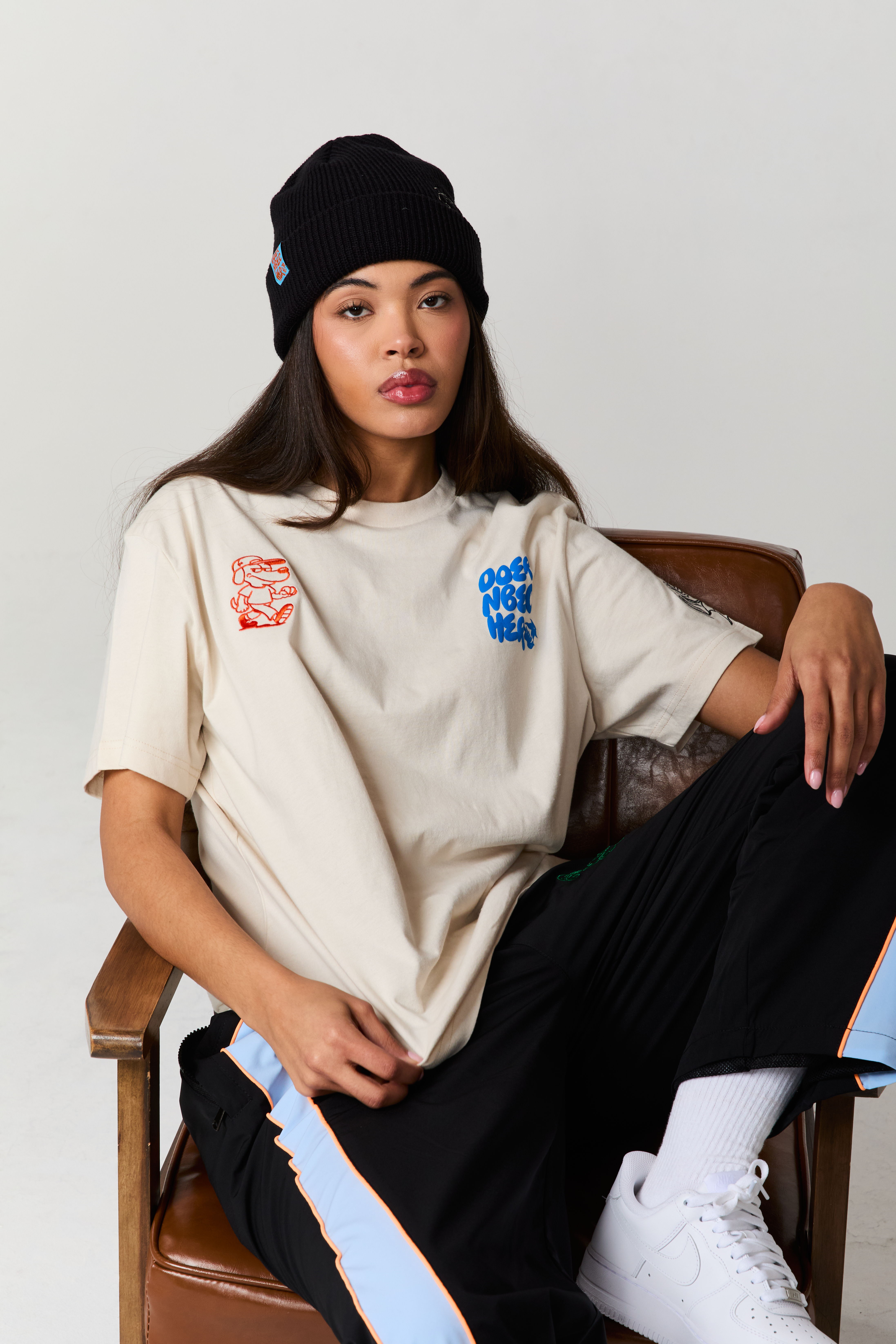 Person wearing a beige shirt and black beanie, sitting on a chair.