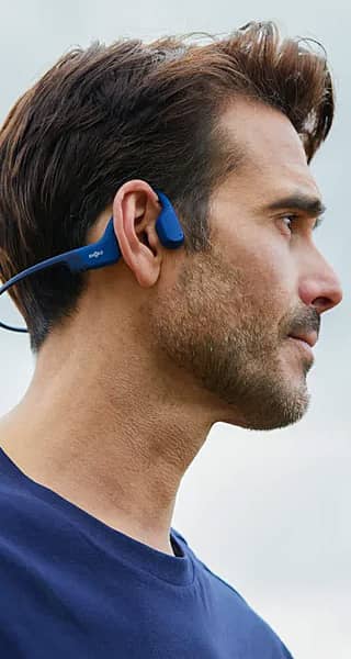 Profile view of a man wearing blue wireless headphones outdoors.