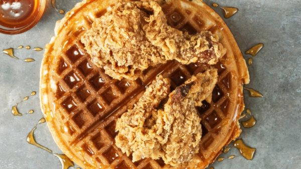 A crunchy drumstick and fried chicken wing on top of a waffle with maple syrup drizzled on top