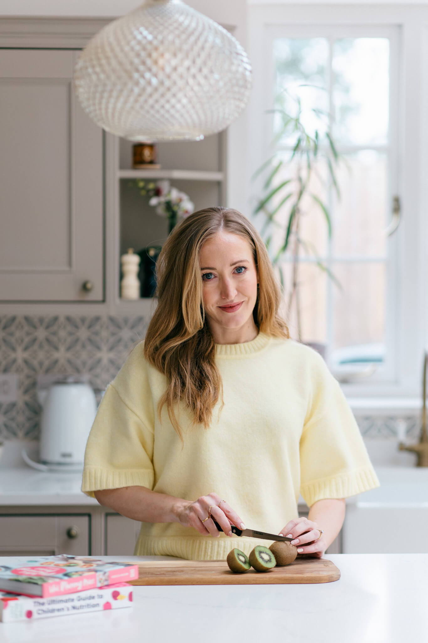 Woman in a yellow sweater preparing food in a bright kitchen.