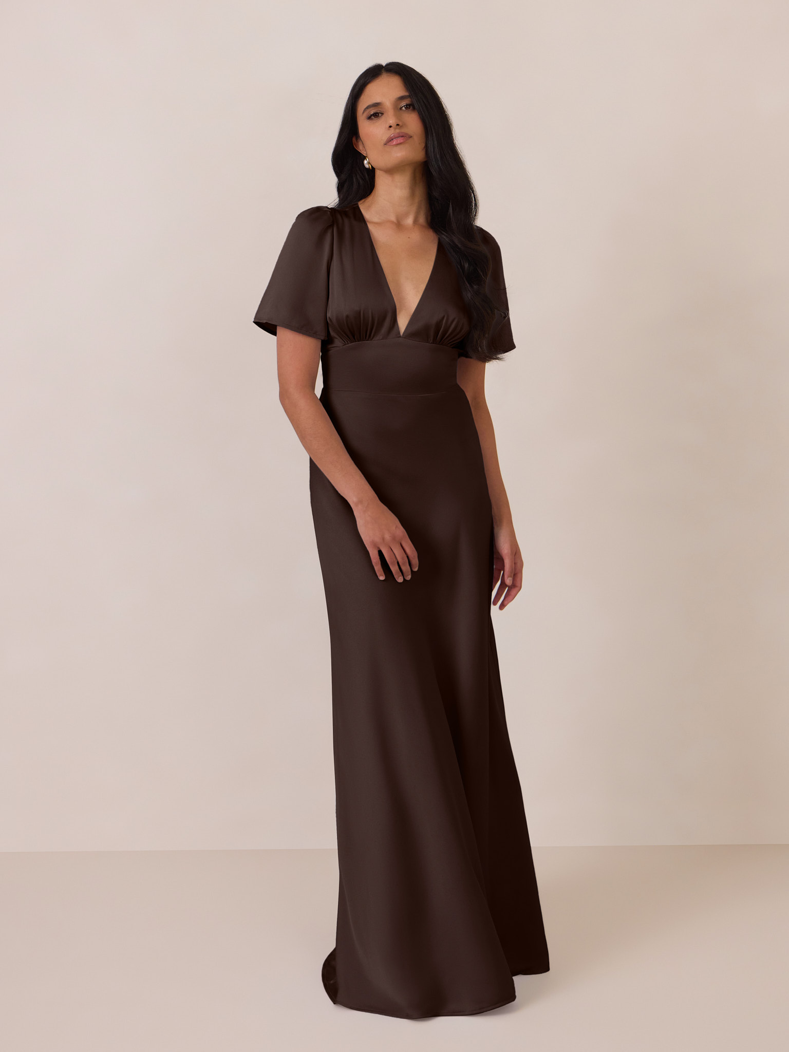 A woman wearing a brown evening gown against a neutral background.
