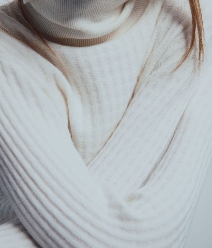 Person wearing a white ribbed sweater with crossed arms.