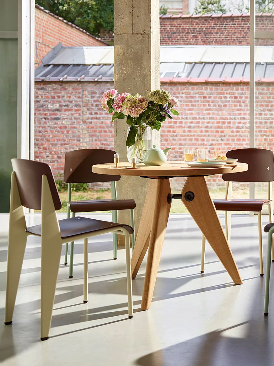 A wooden VITRA table with chairs and a vase of flowers in a bright room.