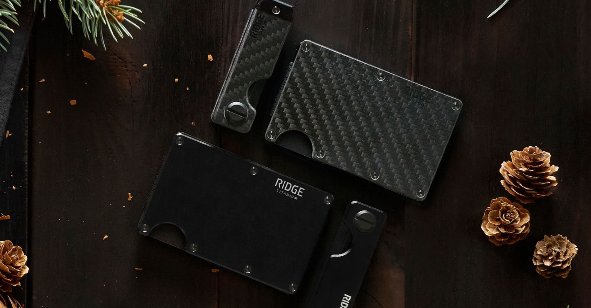 Three stylish wallets on a wooden surface with pinecones and greenery.