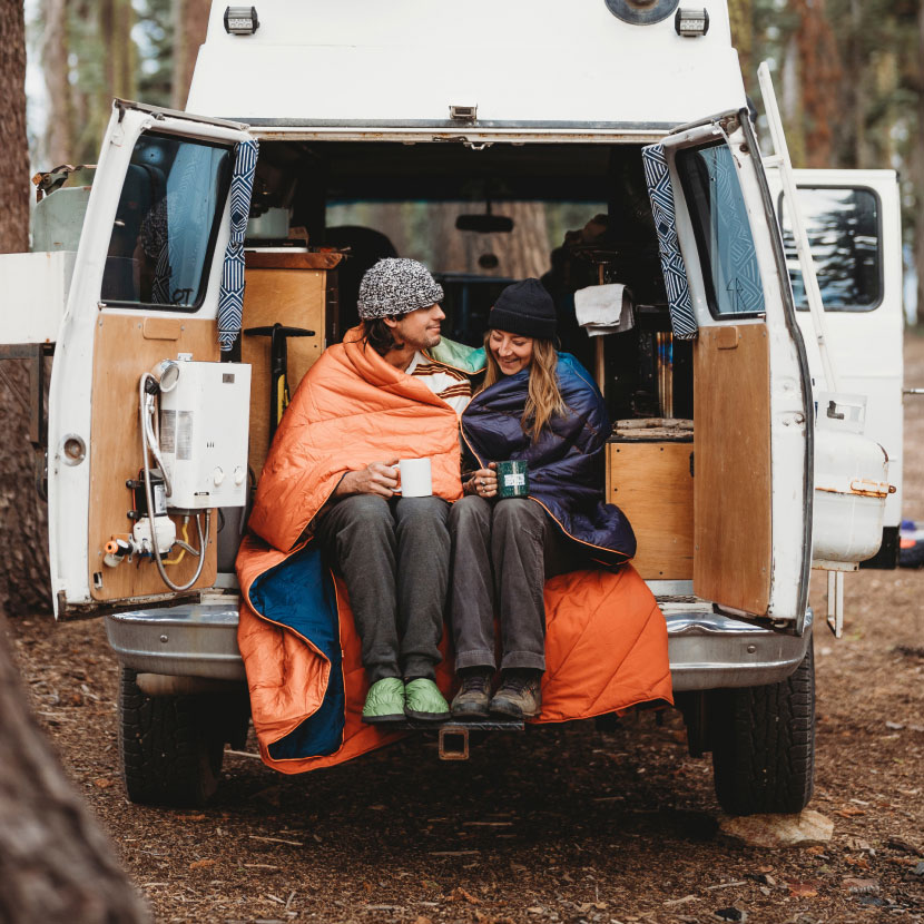 Couple sitting in a van, wrapped in blankets, enjoying nature.