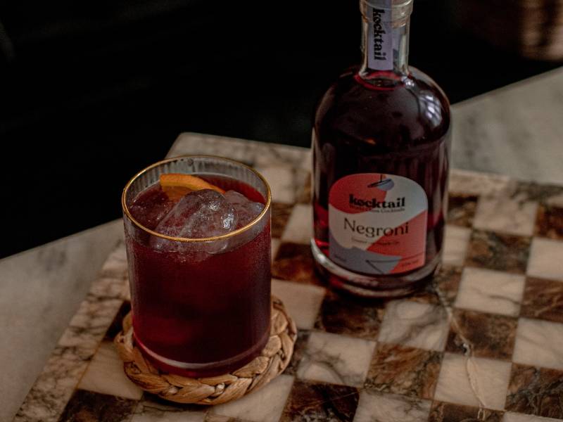 Negroni cocktail in a gold rimmed glass and bottle on a checkered table